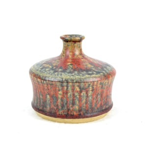 Puede incluir: Un jarrón pequeño, redondo y de cerámica con cuello estrecho. El jarrón está decorado con un esmalte moteado en tonos rojos, marrones y grises.