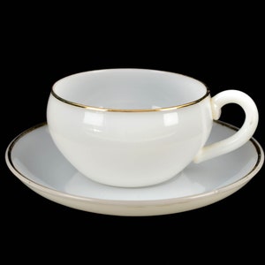 May include: A white teacup with a gold rim sits on a matching saucer. The cup and saucer are both made of porcelain.