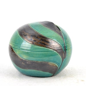 May include: A round ceramic vase with a green glaze and black and brown stripes. The vase has a wide opening at the top.