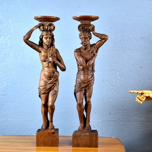 Puede incluir: Un par de esculturas de madera de un hombre y una mujer, cada uno sosteniendo una bandeja en la cabeza. Las esculturas est&aacute;n talladas en un estilo realista y est&aacute;n pintadas en un tono de madera natural.