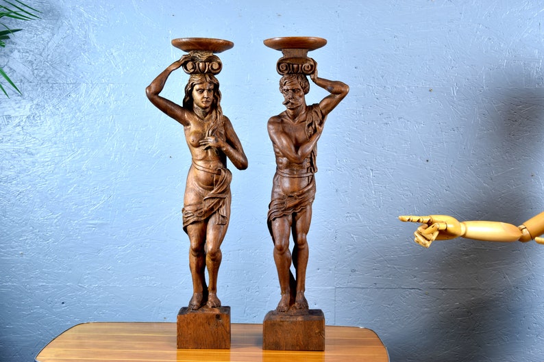 Puede incluir: Un par de esculturas de madera de un hombre y una mujer, cada uno sosteniendo una bandeja en la cabeza. Las esculturas est&aacute;n talladas en un estilo realista y est&aacute;n pintadas en un tono de madera natural.