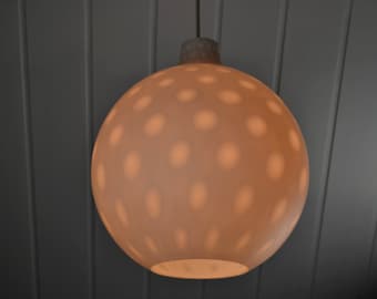 May include: A white, round, ceiling light fixture with a pattern of small, evenly spaced circles. The light is on and casting a warm glow.