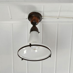 Op de afbeelding: Een witte glazen plafondlamp met een bruine metalen basis en een zwarte metalen rand. De lamp hangt aan een wit plafond.