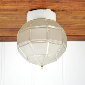 May include: A white ceiling light fixture with a geometric glass shade. The shade is made of frosted glass and has a geometric pattern.
