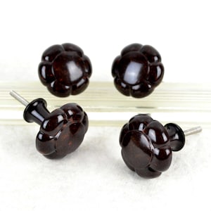 Può includere: Quattro pomelli per armadio di colore marrone a forma di fiore con una vite argentata. I pomelli hanno una superficie testurizzata, leggermente irregolare.