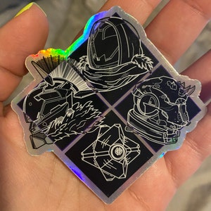 May include: A holographic sticker featuring four Destiny game character designs. The sticker has a black background with white line art of the characters. The sticker is held in a hand and has a rainbow sheen.