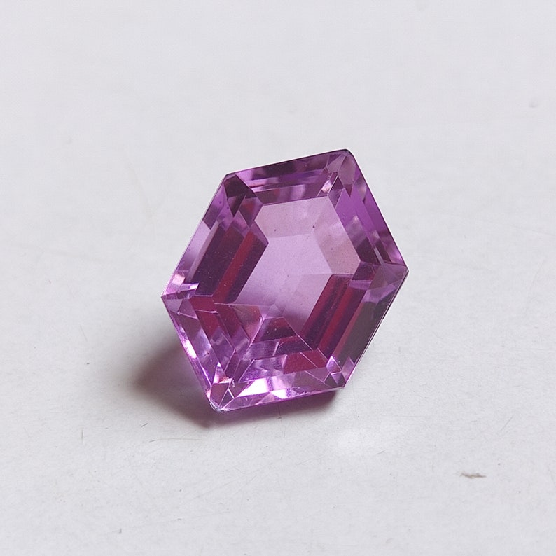 May include: A hexagonal cut amethyst gemstone with a purple hue.