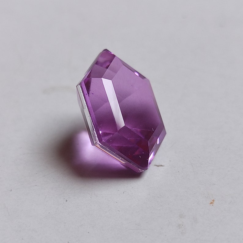 May include: A purple faceted glass gem with a hexagonal shape.