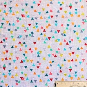 Könnte beinhalten: Weißer Stoff mit einem sich wiederholenden Muster aus kleinen, bunten Dreiecken. Die Dreiecke sind in den Farben Rot, Orange, Gelb, Grün, Blau und Grau.