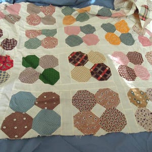 May include: A patchwork quilt featuring an off-white fabric base with repeating octagonal fabric patches in various colors and patterns, including red, green, yellow, brown, and blue floral, plaid, and polka dot designs arranged in a grid.