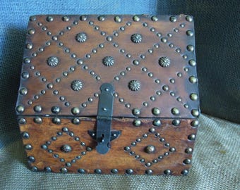 May include: A rectangular wooden chest with a hinged lid, featuring a dark brown finish. The exterior is decorated with a diamond pattern of small metal studs and larger circular metal accents. A black metal latch secures the front.