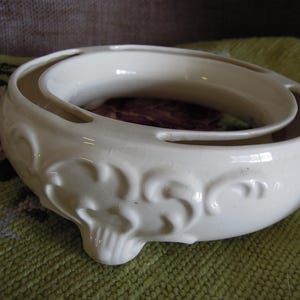 May include: White ceramic planter with a decorative design. The planter has two tiers and is designed to hold a plant or flowers.