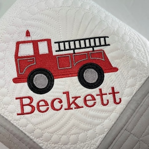 May include: White quilted baby blanket with a red fire truck and the name Beckett embroidered in red.