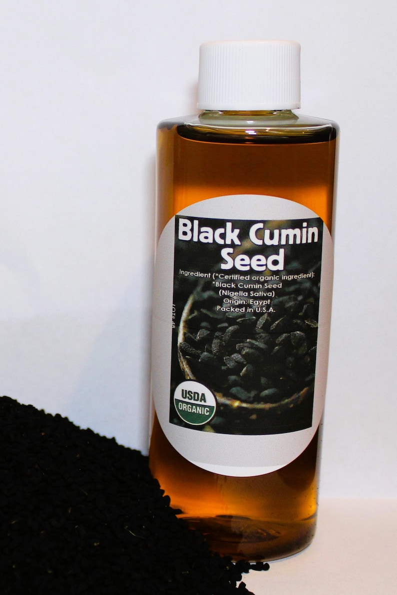 Puede incluir: Una botella de vidrio de aceite de semilla de comino negro org&aacute;nico certificado por la USDA. La botella tiene una etiqueta blanca con texto negro que dice "Semilla de comino negro" y enumera los ingredientes como "Ingrediente org&aacute;nico certificado) "Semilla de comino negro (Nigella Sativa) Origen: Egipto Envasado en EE. UU.". La botella est&aacute; sobre un mont&oacute;n de semillas de comino negro.