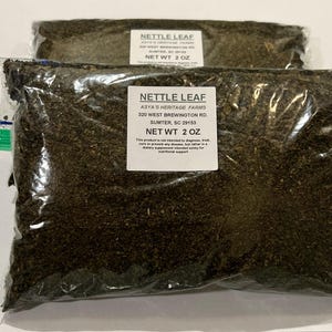 May include: Two clear plastic bags filled with dried nettle leaf. Each bag has a white label with the text "NETTLE LEAF" and "NET WT 2 OZ". The bags are sealed and appear to be ready for sale.