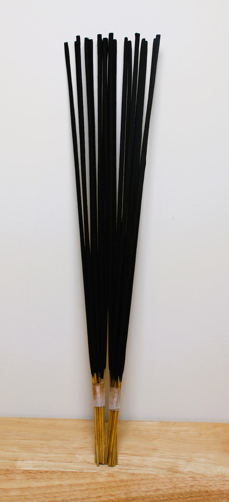 May include: A bundle of black incense sticks with a golden base. The sticks are tied together with a clear band.