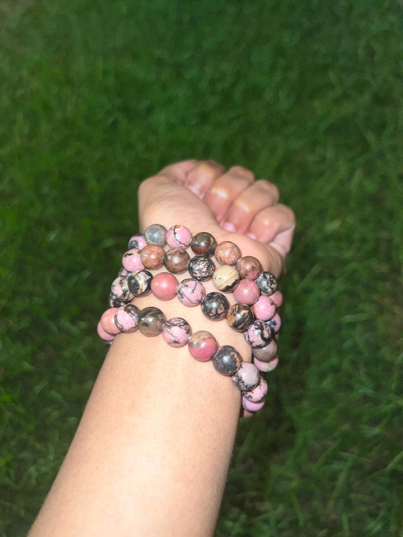 May include: Several beaded bracelets with pink, brown, and gray stones. The bracelets are stacked on top of each other. The beads are round and appear to be made of natural stone.