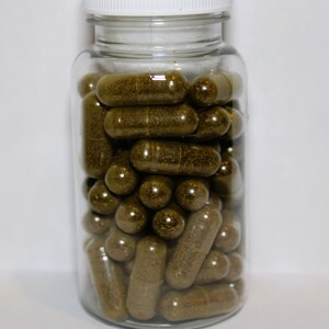 May include: A clear glass jar filled with brown capsules. The jar has a white lid.