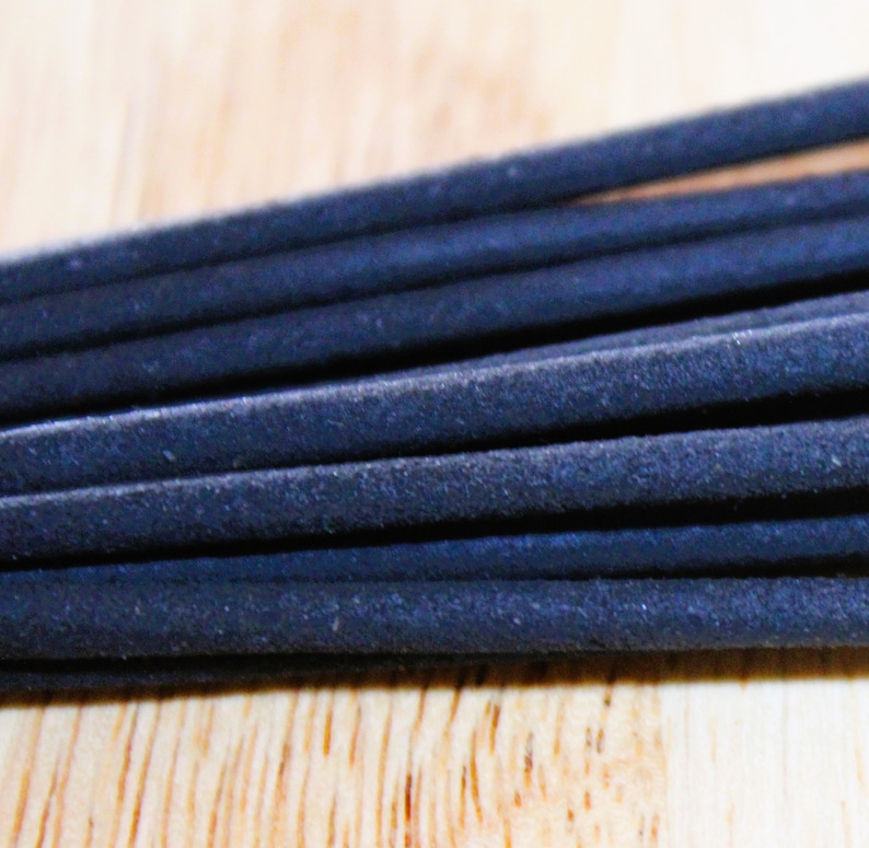 May include: A close-up of a bundle of black incense sticks. The sticks are arranged in a neat stack, with the ends of the sticks visible.