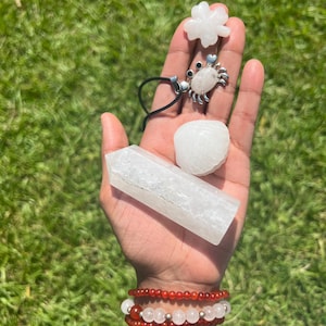 Peut inclure: Une collection de cristaux blancs et transparents comprenant une forme de trèfle à quatre feuilles, un pendentif en forme de crabe sur un cordon noir, une pierre lisse arrondie et une pointe hexagonale. Deux bracelets de perles rouges et blanches.