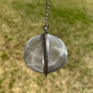 May include: A stainless steel tea infuser with a chain. The infuser is spherical, made of fine mesh, and designed to hold loose tea leaves. The chain allows for easy removal from a cup or teapot.