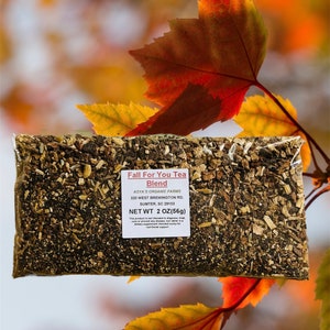 May include: A close-up of a brown paper bag filled with dried herbs and labeled "Fall For You Tea Blend". The bag is sitting on a table with a blurred background of fall leaves.
