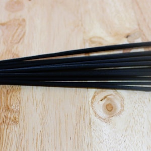 May include: A bundle of black incense sticks with gold and white accents. The sticks are arranged in a row on a wooden surface.