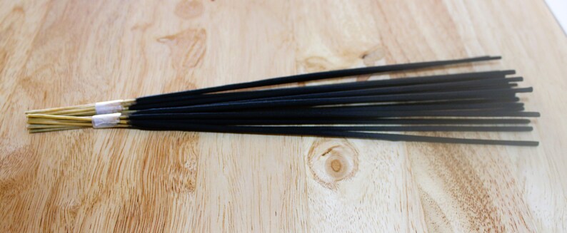 May include: A bundle of black incense sticks with gold and white accents. The sticks are arranged in a row on a wooden surface.