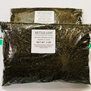 Könnte beinhalten: Zwei transparente Plastiktüten gefüllt mit getrockneten Brennnesselblättern. Jede Tüte hat ein weißes Etikett mit der Aufschrift "NETTLE LEAF" und "NET WT 2 OZ". Die Etiketten zeigen auch die Adresse von Asya's Heritage Farms in Sumter, SC.