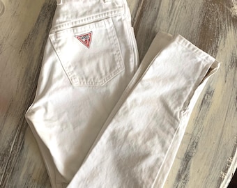 May include: White high-waisted jeans with a Guess logo on the back pocket.