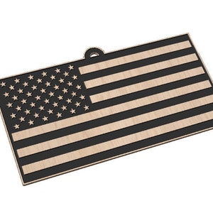 May include: A wooden American flag ornament with a black and natural wood color scheme. The flag features 50 stars in the upper left corner and 13 stripes. The ornament has a small hole at the top for hanging.