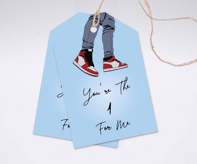 May include: Two pale blue gift tags featuring an illustration of legs in grey jeans and red, white, and black trainers. The tags have the text "You're the 1 For Me" in black script.
