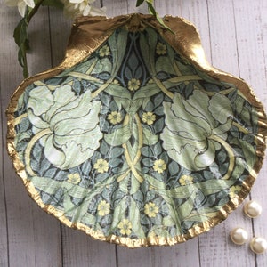 May include: A decorative seashell dish with a gold-painted rim. The interior features a floral pattern in shades of green, blue, and yellow. The dish is adorned with a botanical design, and is a unique home decor item.
