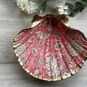 May include: A decorative seashell dish with a pink and white floral pattern and gold trim.