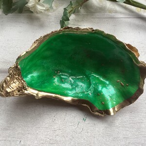 May include: A green oyster shell dish with gold accents. The shell is smooth and shiny, and the gold accents are on the edges of the shell.