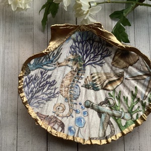 May include: A white seashell dish with a gold rim, featuring a seahorse, coral, and an anchor. The dish is decorated with a blue, green, and brown colour scheme.