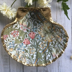 May include: A decorative seashell-shaped dish with a gold-painted rim. The interior features a floral pattern with pink, blue, and yellow flowers on a white background. The dish is likely used for holding small items.