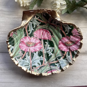 May include: A decorative seashell-shaped dish with a gold-painted rim. The interior features a floral design with pink poppies and green leaves on a dark green background. A unique home decor item.