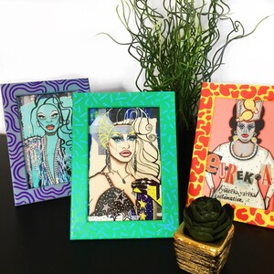 May include: Three framed illustrations of drag queens. The frames are painted in different patterns: purple and blue swirls, green and turquoise dashes, and yellow and orange animal print. The illustrations are of drag queens with colorful makeup and costumes. The text in the bottom right frame reads "Eureka!" and "your play, your reclamation."
