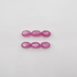 May include: Six oval-shaped pink gemstones on a white background.