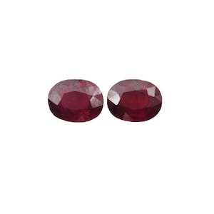 May include: Two oval-shaped, red gemstones. The gemstones are faceted and have a slightly translucent appearance.