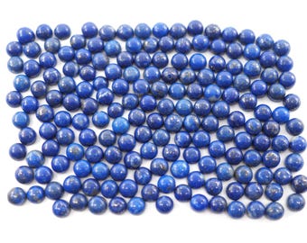 Puede incluir: Una colección de pequeñas piedras preciosas redondas de lapislázuli pulido. Las piedras son de un color azul intenso y rico con sutiles variaciones de tono y textura. Están dispuestas juntas sobre un fondo blanco.