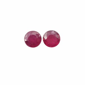 May include: Two round, red gemstones with a faceted cut.