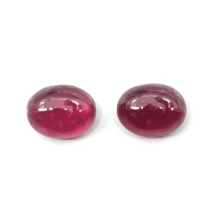May include: Two oval-shaped, cabochon cut, red gemstones. The gemstones are smooth and polished.