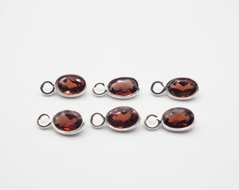May include: Six silver oval-shaped charms with red gemstone accents. Each charm has a small loop for attaching to a necklace or bracelet.