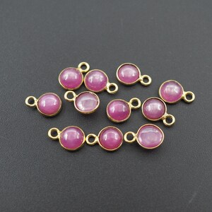 Puede incluir: Hallazgos de joyería de metal dorado con piedras preciosas redondas de color magenta. Los hallazgos tienen un lazo a cada lado para unirlos a otros componentes. Las piedras preciosas están engastadas en un engaste de bisel.