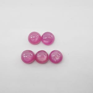 May include: Five pink cabochon gemstones, each with a smooth, rounded surface. The stones are arranged in a row, with three in the center and two on either side.