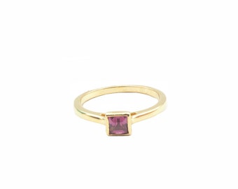 Puede incluir: Un anillo de oro con una piedra preciosa de color púrpura de forma cuadrada.