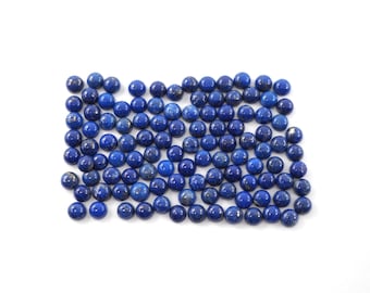 Puede incluir: Una colección de gemas redondas y pulidas de lapislázuli. Las gemas son de un color azul profundo y rico con sutiles variaciones de tono. Están dispuestas juntas sobre un fondo blanco, mostrando sus superficies lisas.