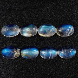Könnte beinhalten: Acht ovale Mondstein-Cabochons mit einem blauen, irisierenden Schimmer. Die Steine sind in zwei Reihen zu je vier angeordnet.